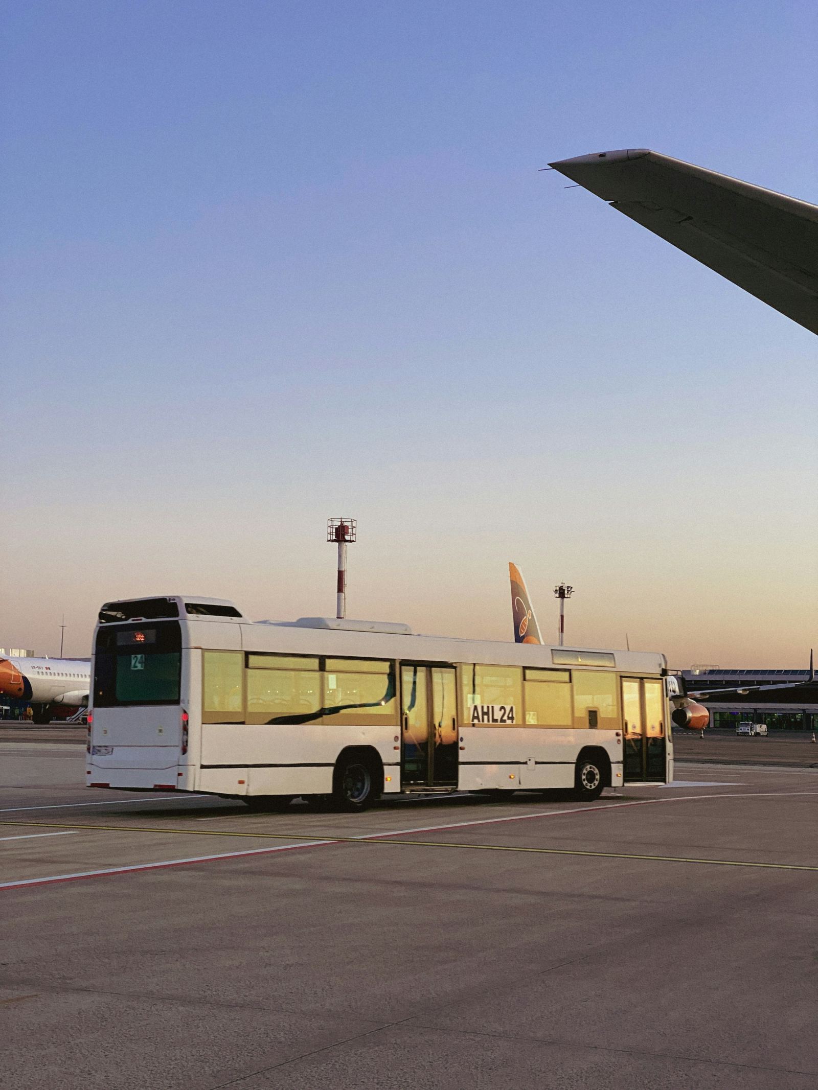 Airport shuttle bus parked on the tarmac beside an aircraft wing at dusk