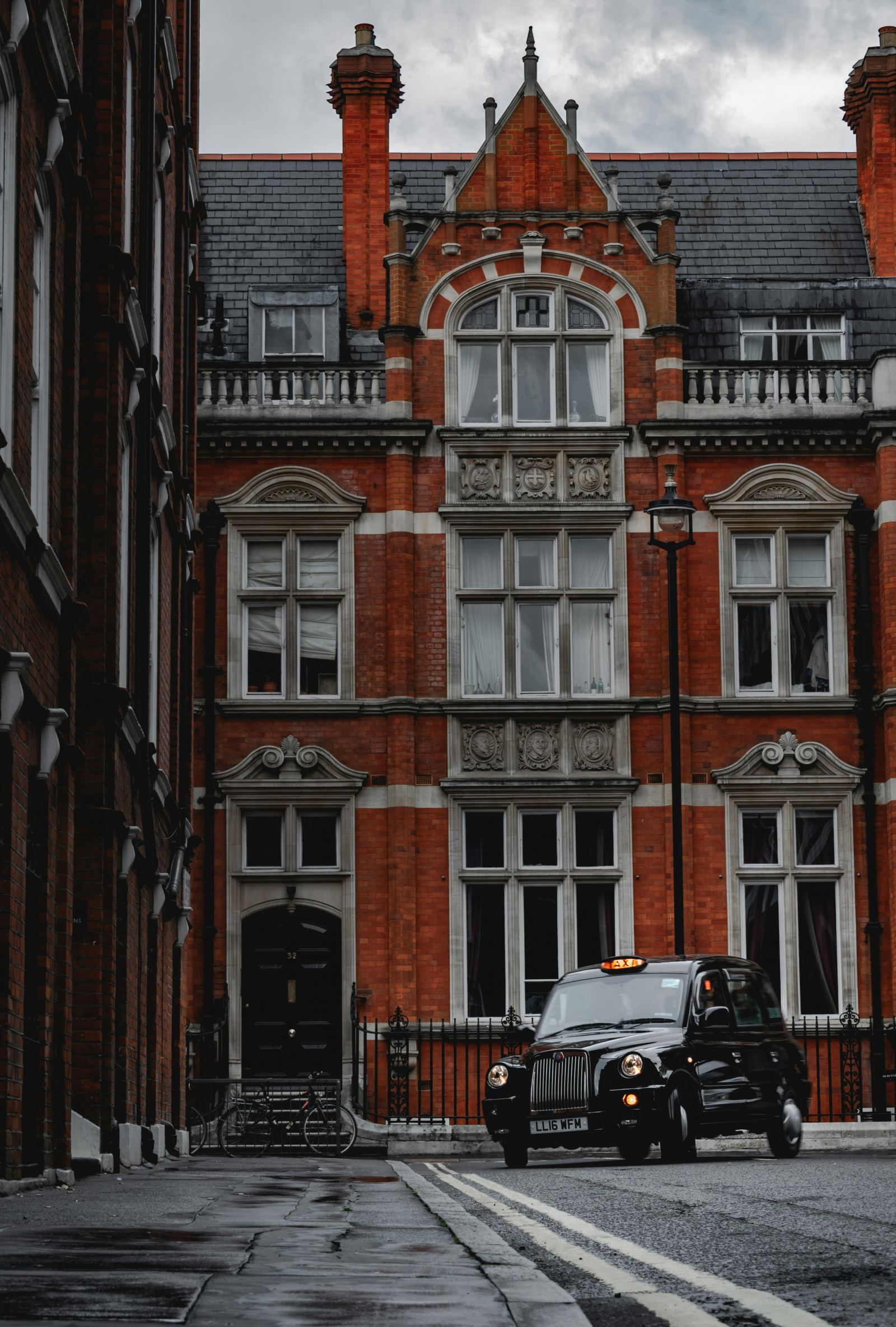 Black London taxi parked in front of a red-brick Victorian townhouse