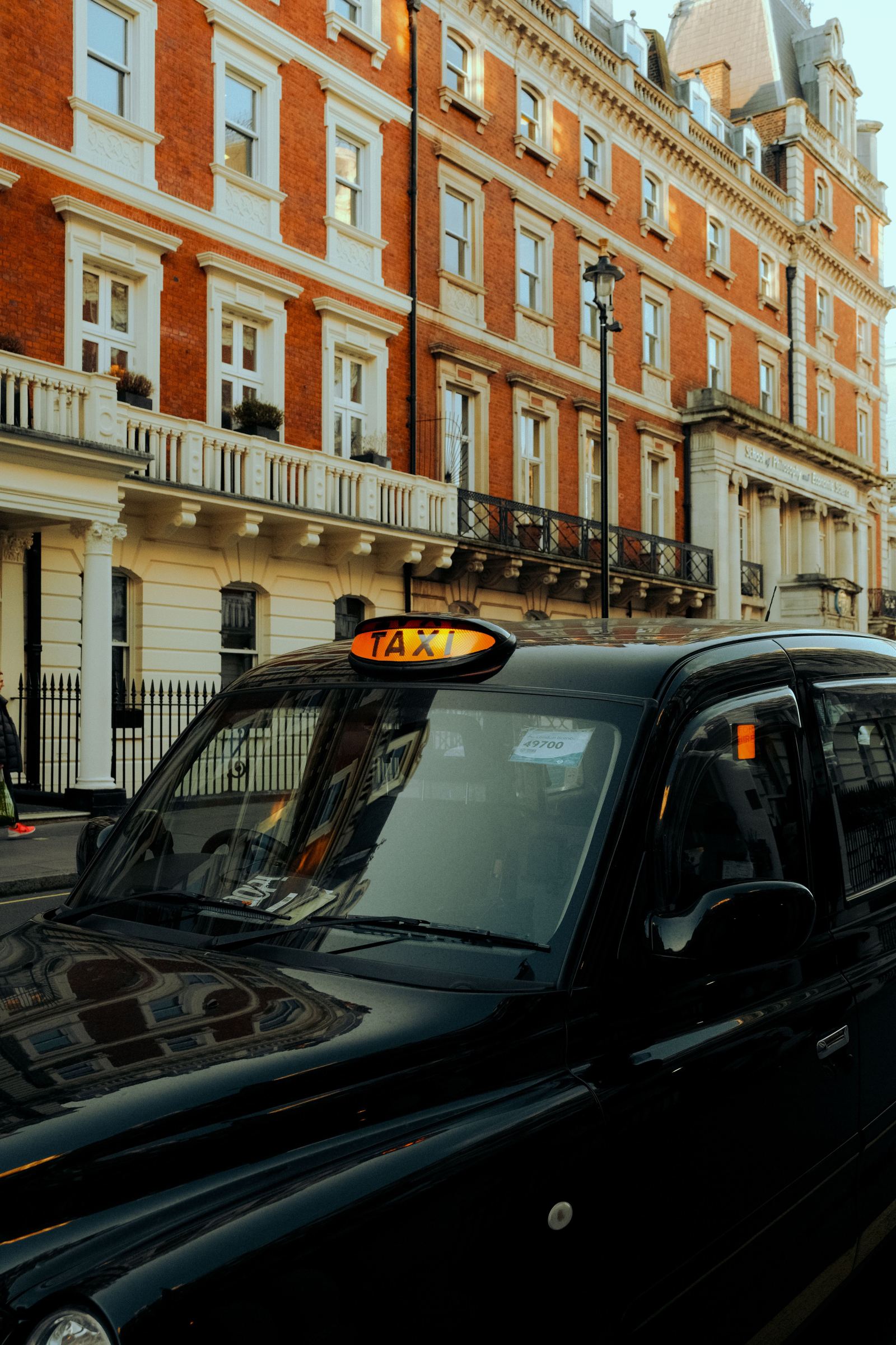 London taxi with an illuminated TAXI roof sign parked on a brick-fronted street