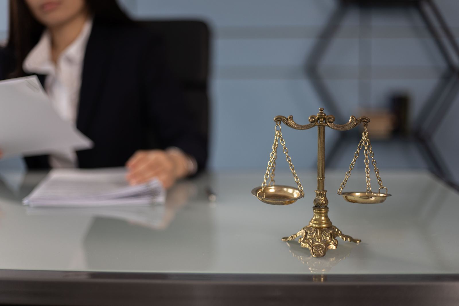 Small brass scales of justice balanced on a glass office desk