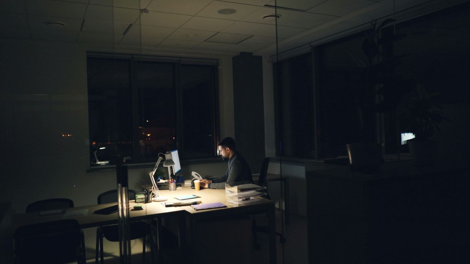 Man working alone at a lamp-lit desk in an otherwise dark office at night