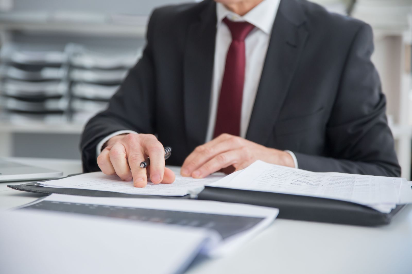 Close-up of a businessman’s hands holding a pen while reviewing paperwork