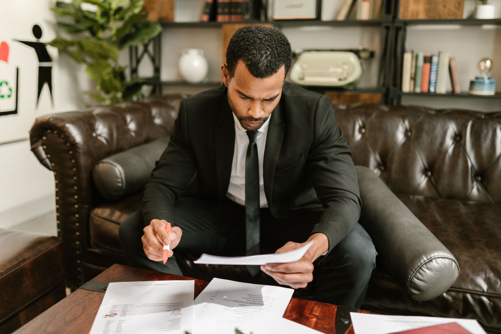 Man in a suit reviewing printed documents while seated on a leather couch