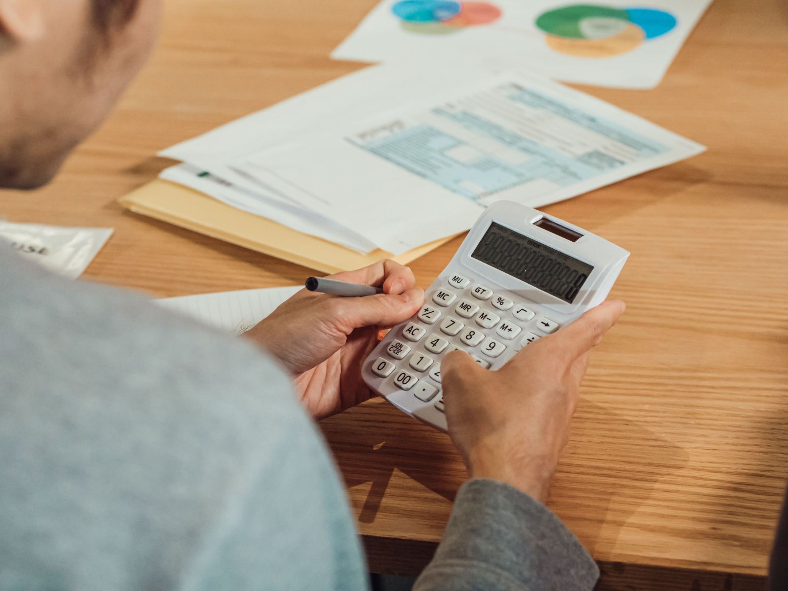 Hands using a calculator beside printed reports with colorful pie charts