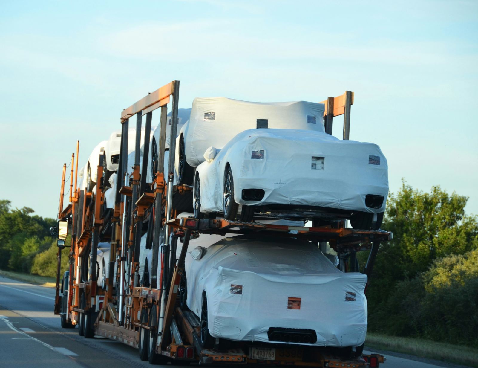 Multi-level car carrier trailer hauling vehicles wrapped in protective covers on a highway