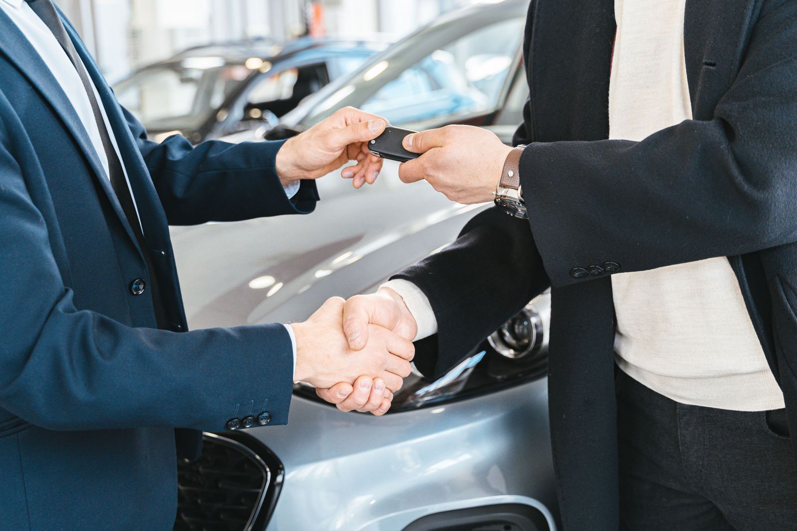 Two men shaking hands while exchanging a car key fob at a dealership