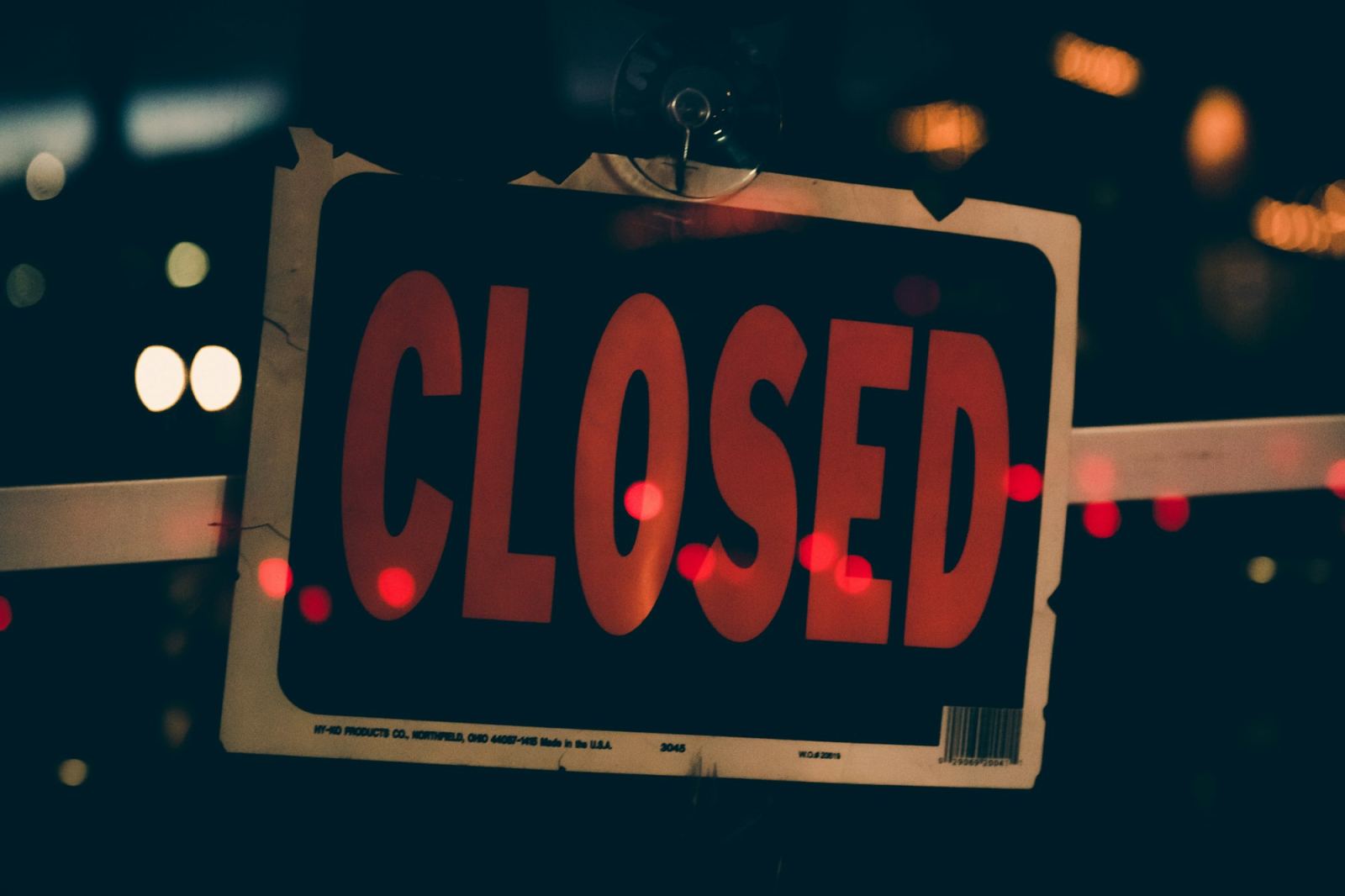 Red CLOSED sign hanging in a window lit by night-time city lights