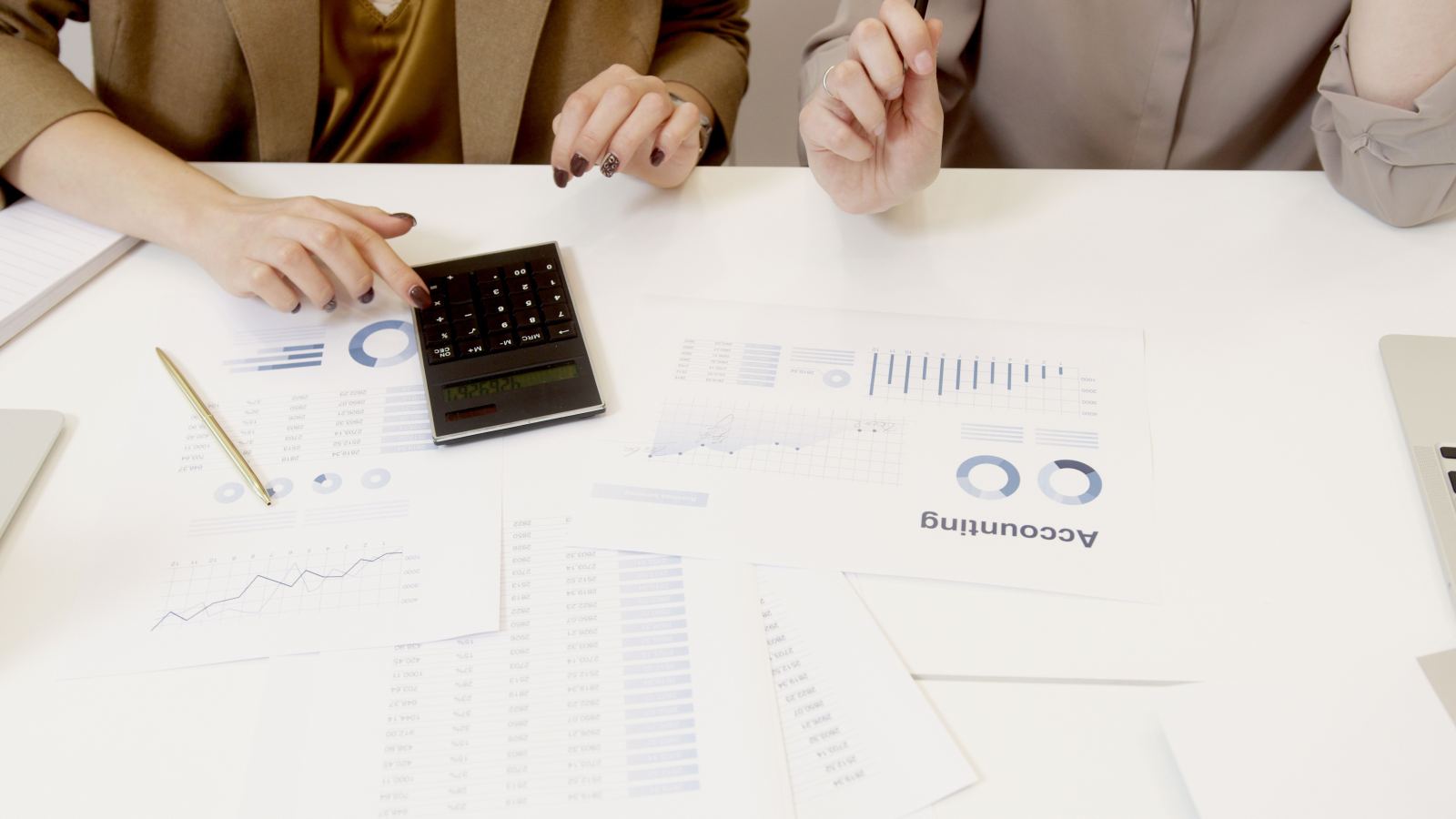 Two colleagues using a calculator beside printed accounting charts on a desk