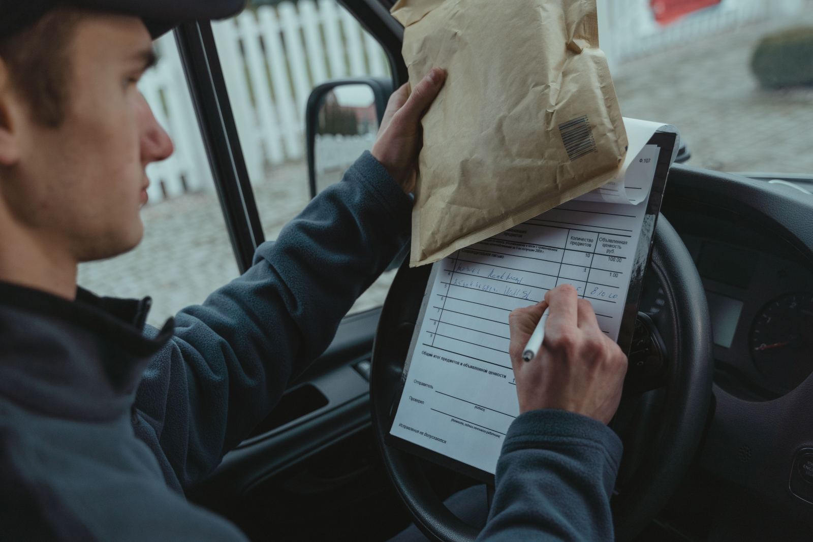 Courier signing a delivery confirmation form on a clipboard inside a vehicle
