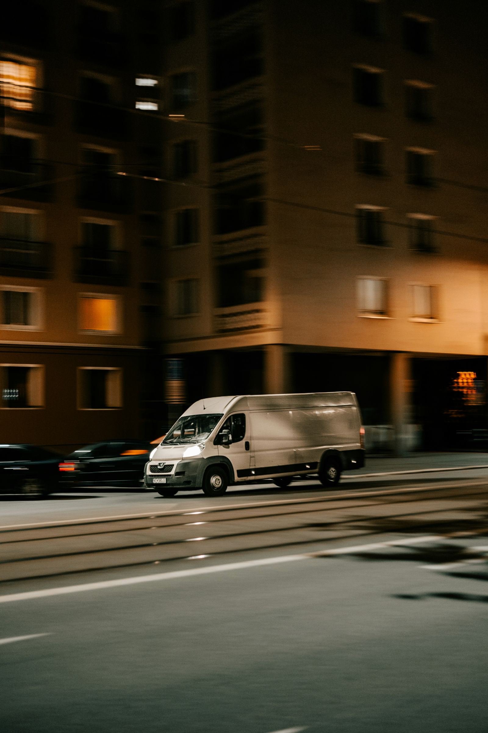 White delivery van driving through a city street at night with motion blur