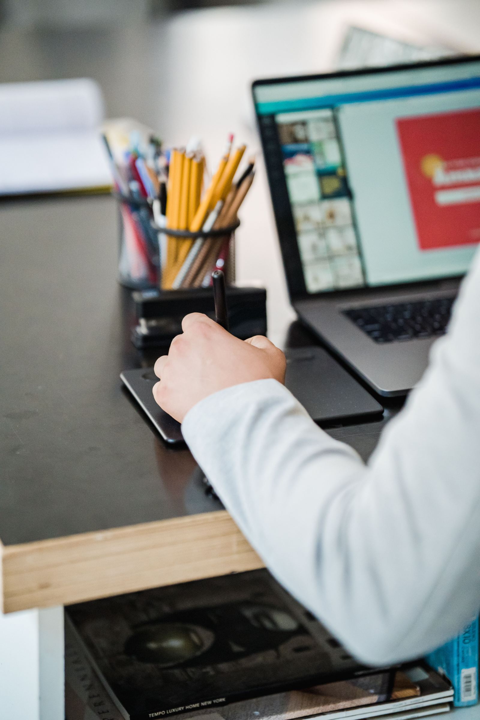 Person using a stylus on a graphics tablet beside an open laptop on a desk