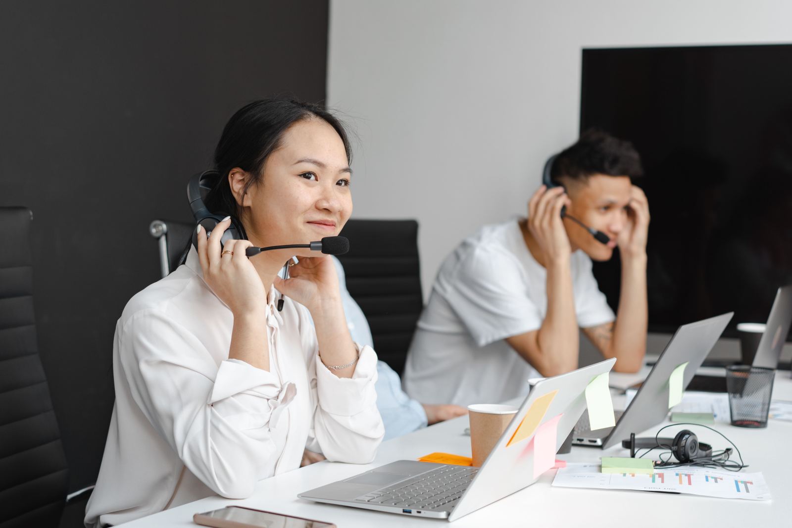 Two call center agents wearing headsets working at laptops in an office