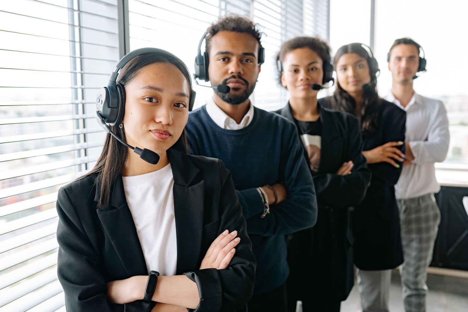 Diverse team of five call answering agents wearing headsets standing together in an office