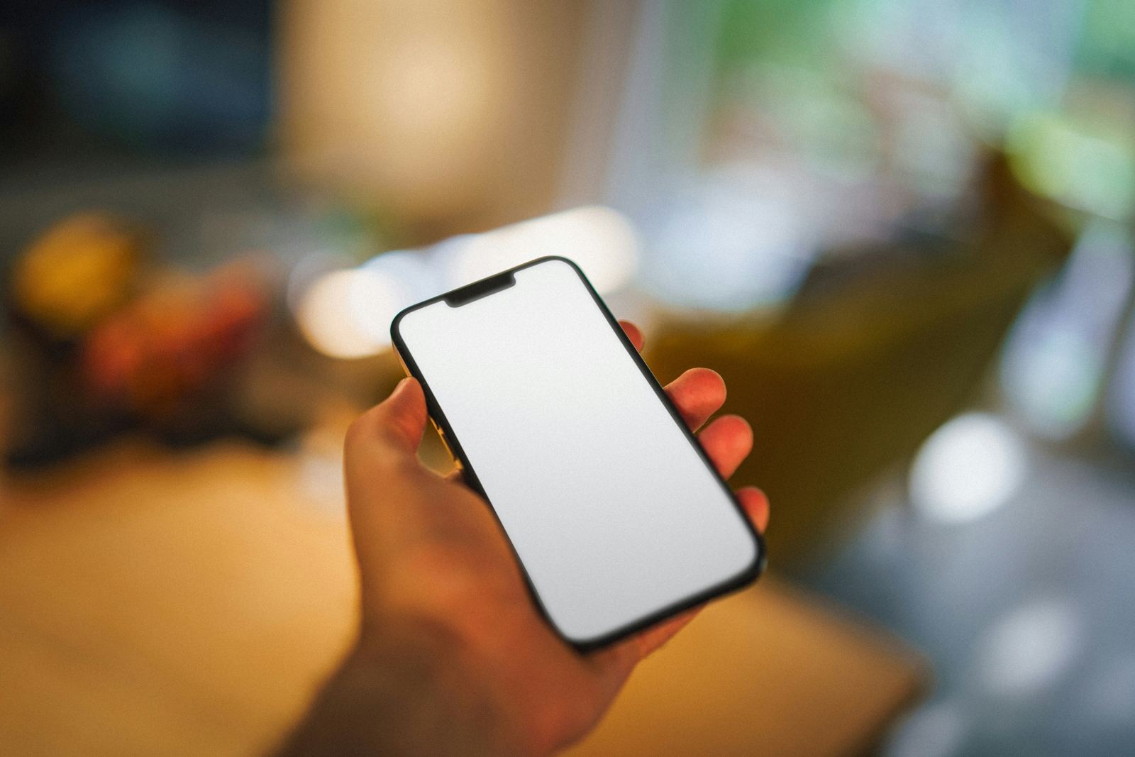 Hand holding a smartphone with a blank screen in a blurred office setting