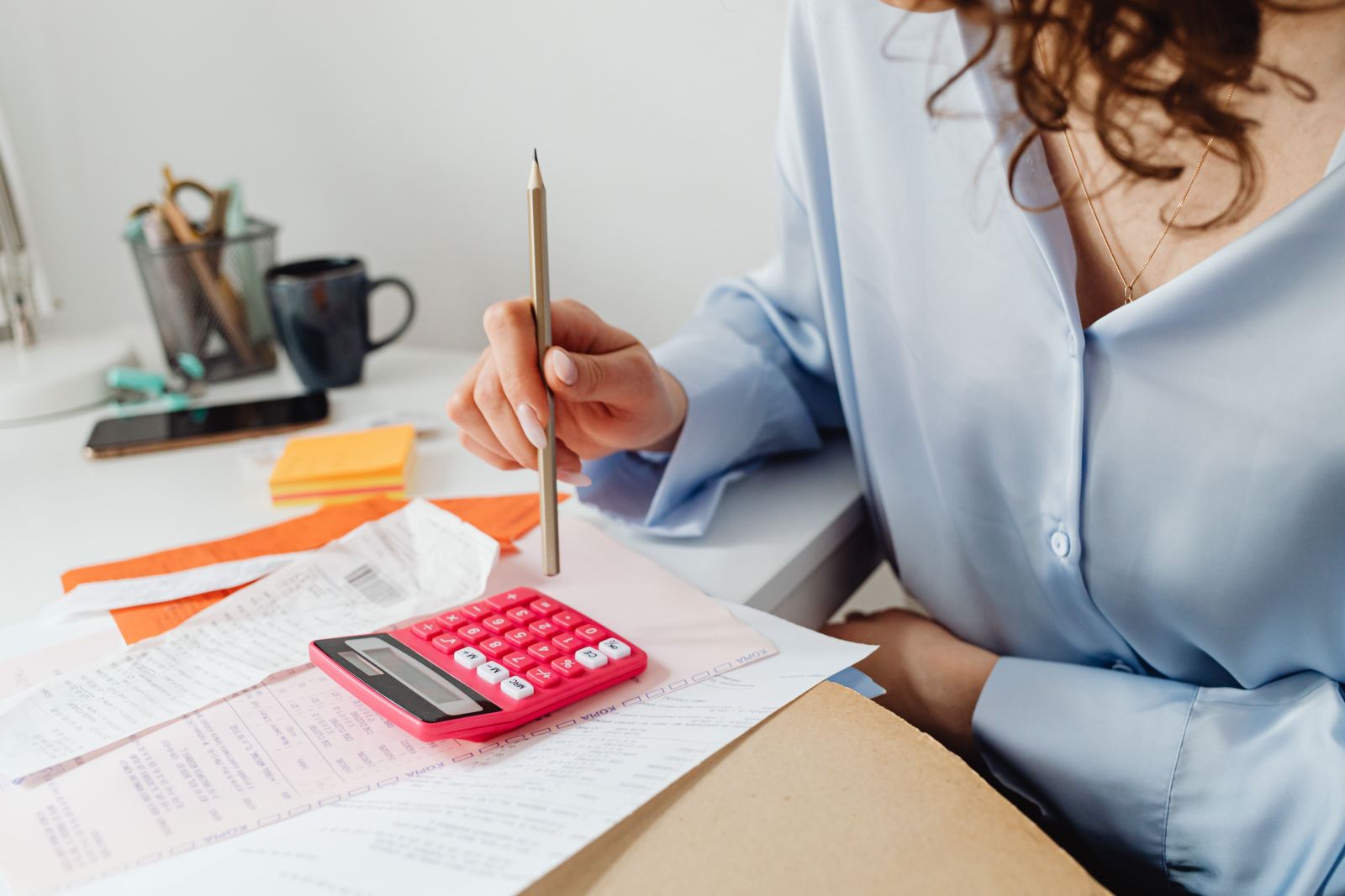 Hand holding a pencil over a calculator and papers on a desk