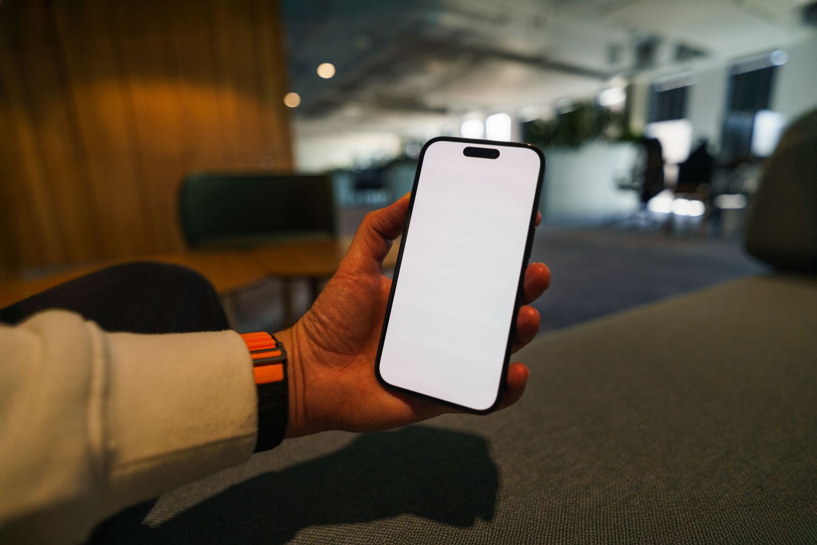 Hand wearing a watch holding a smartphone with a blank screen in an office