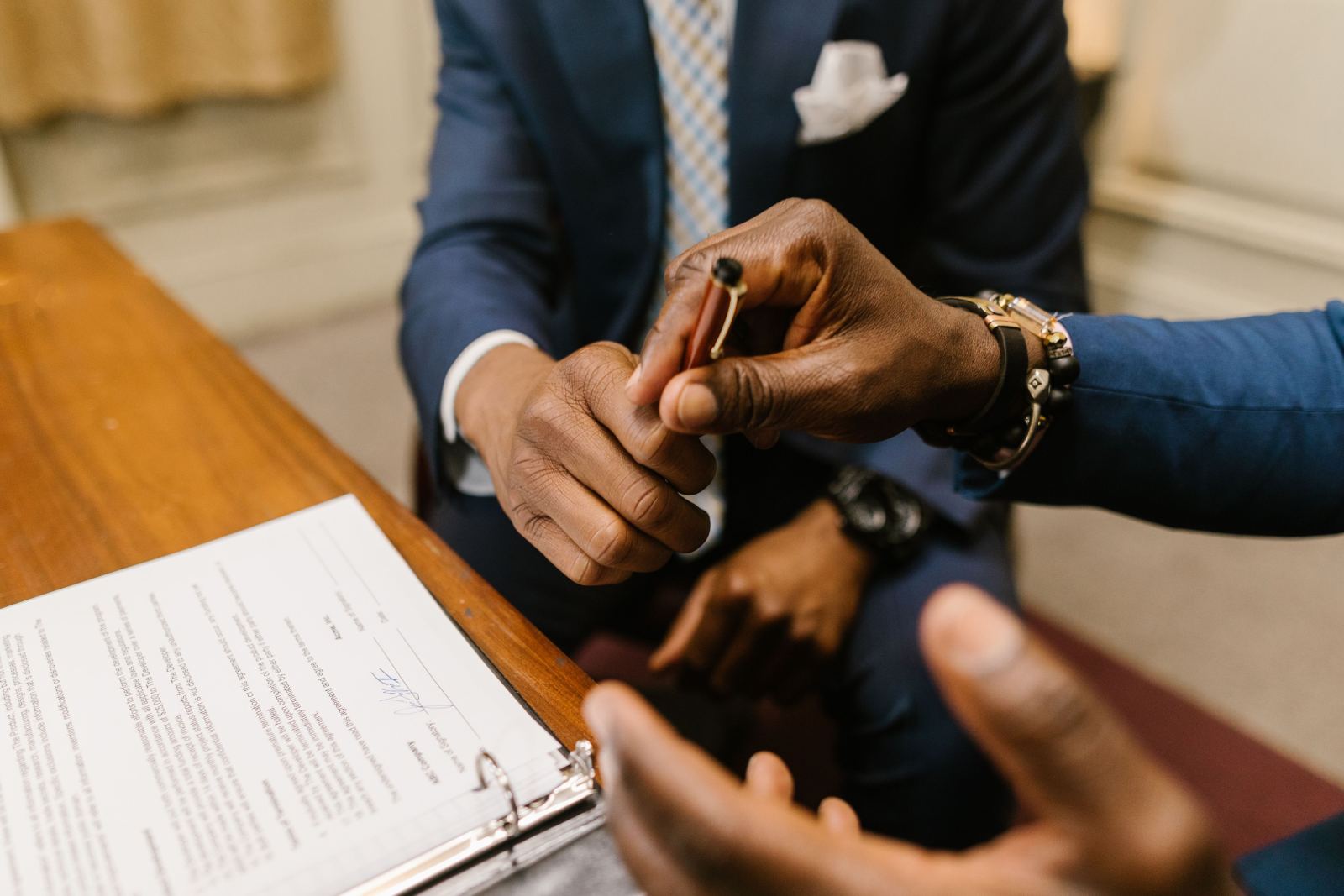Close-up of hands exchanging a pen over a signed contract in a binder