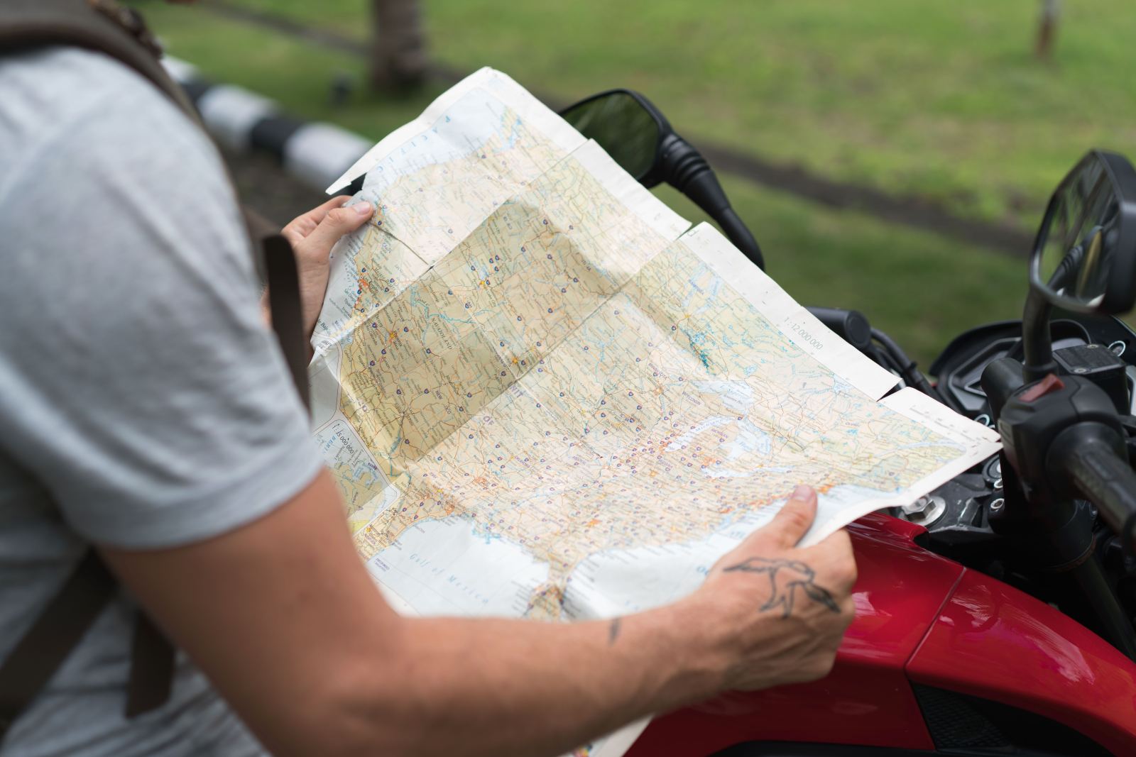 Hands holding open a paper road map beside a parked motorcycle