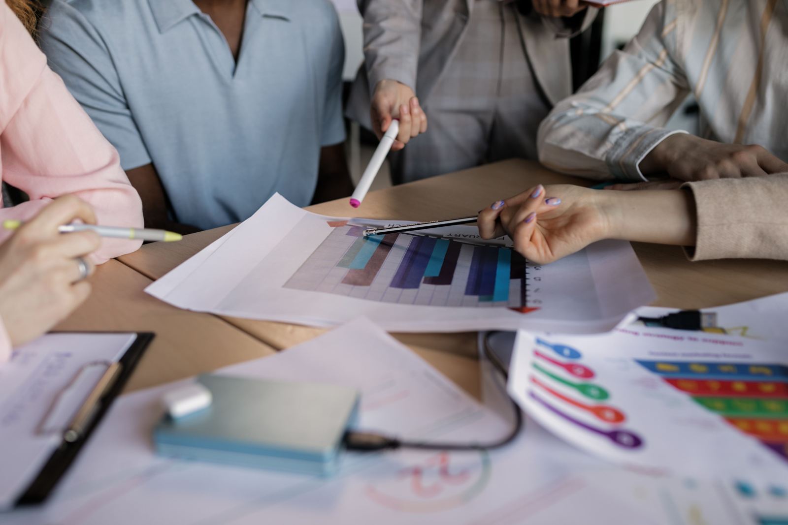 Hands pointing at a colorful bar chart printed on paper during a meeting
