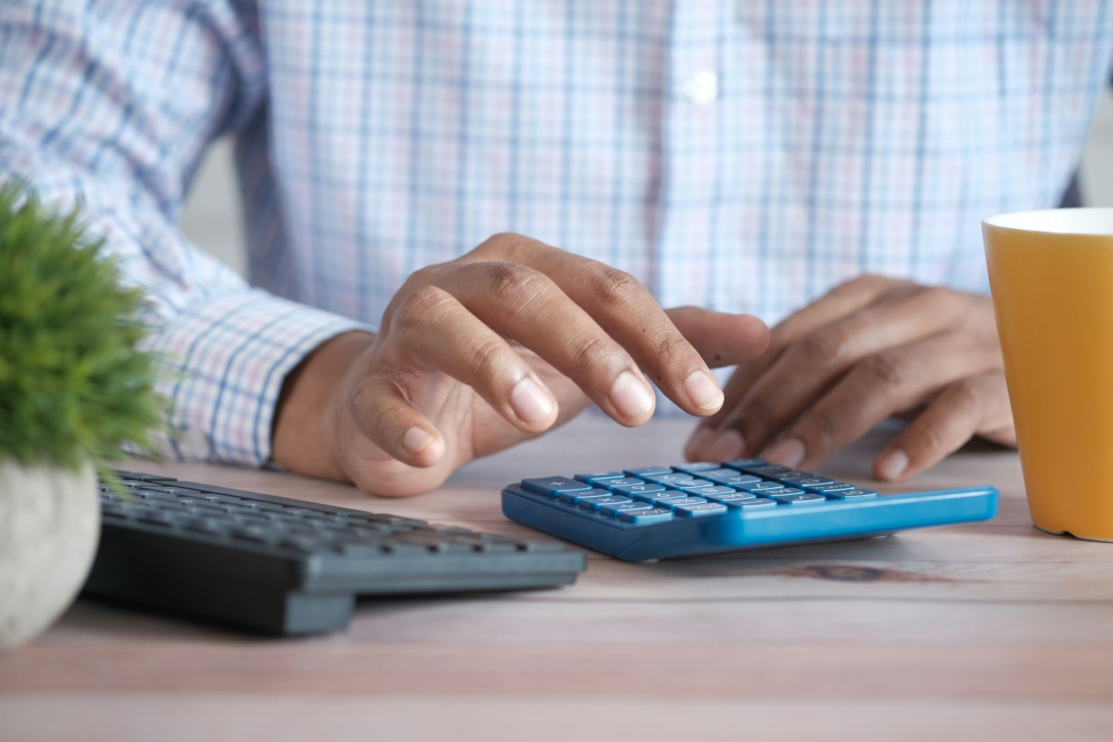 Hands typing on a calculator beside a keyboard on an office desk