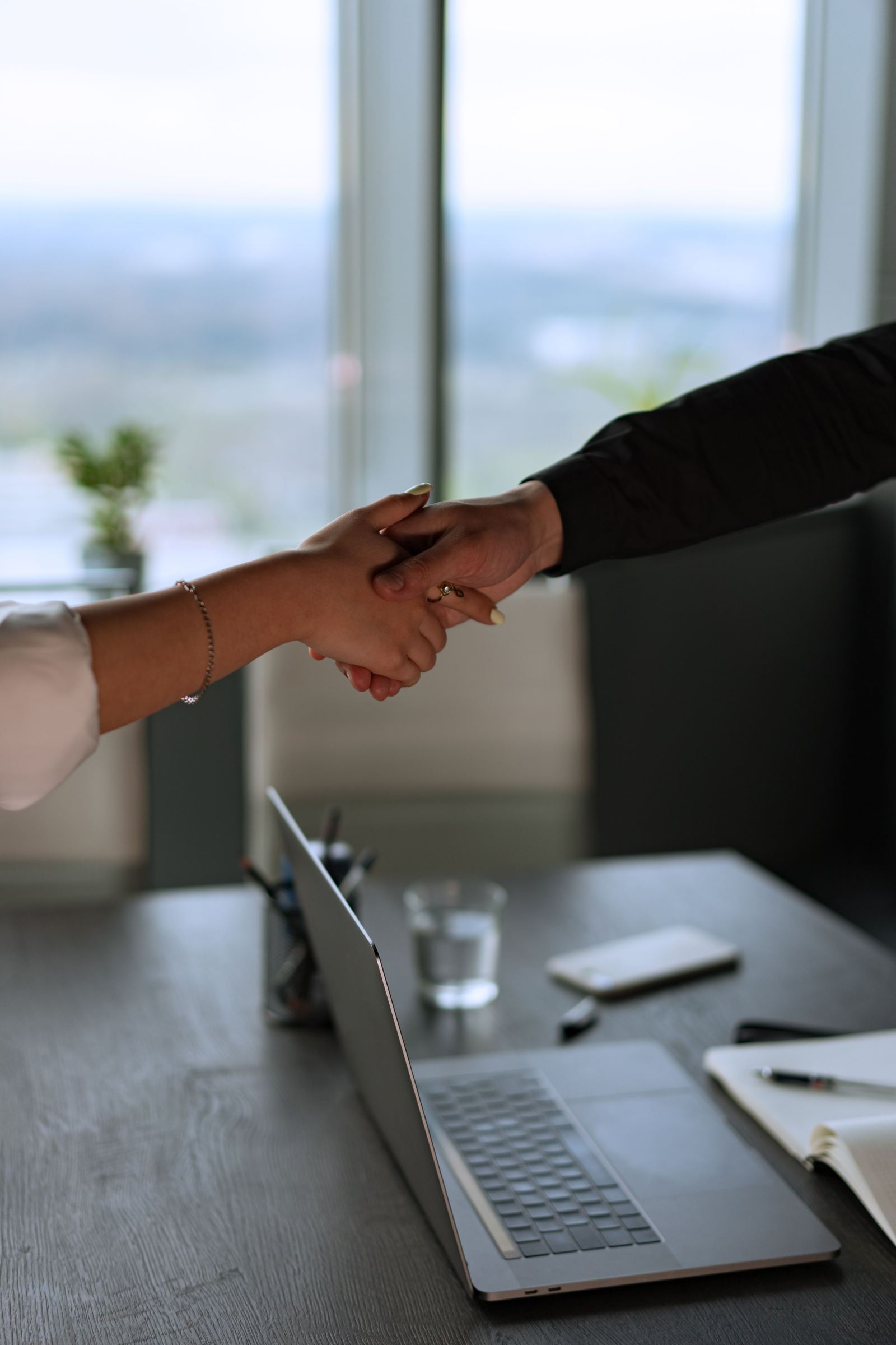 Two people shaking hands in an office with a laptop visible in the blurred background