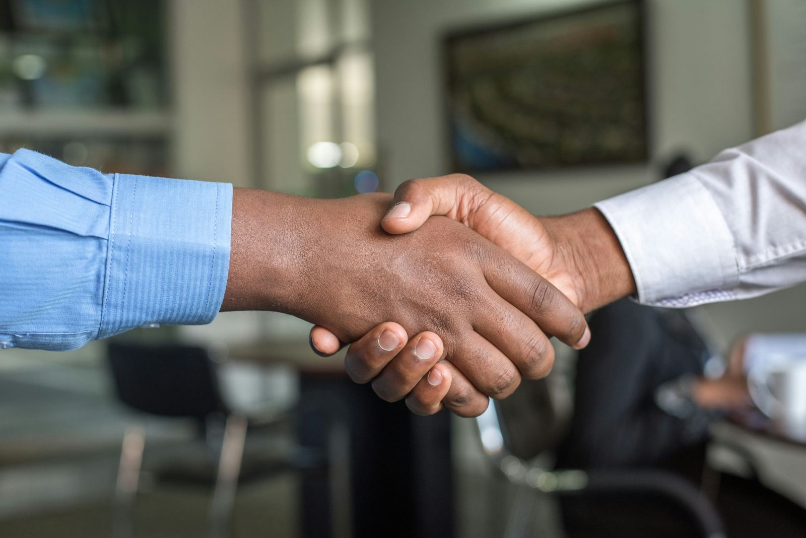 Two people shaking hands in an office with a framed picture on the wall behind them