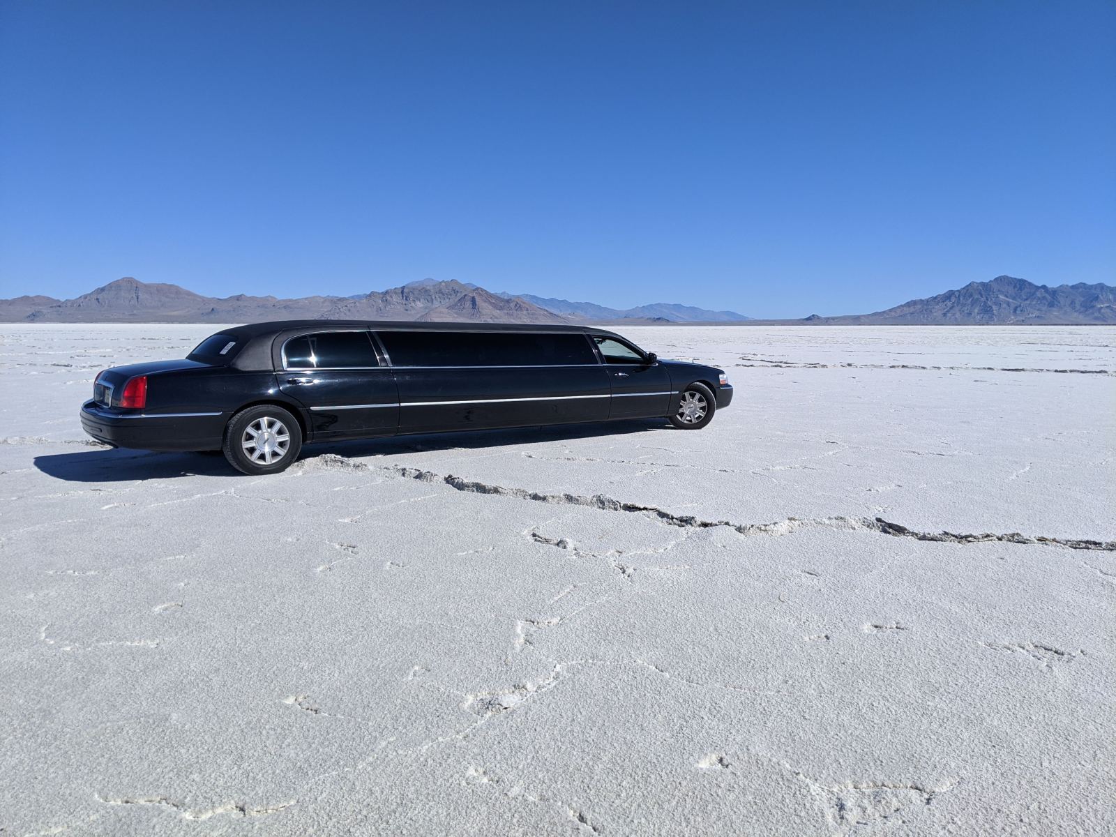 Black stretch limousine parked on a white salt flat with mountains behind it