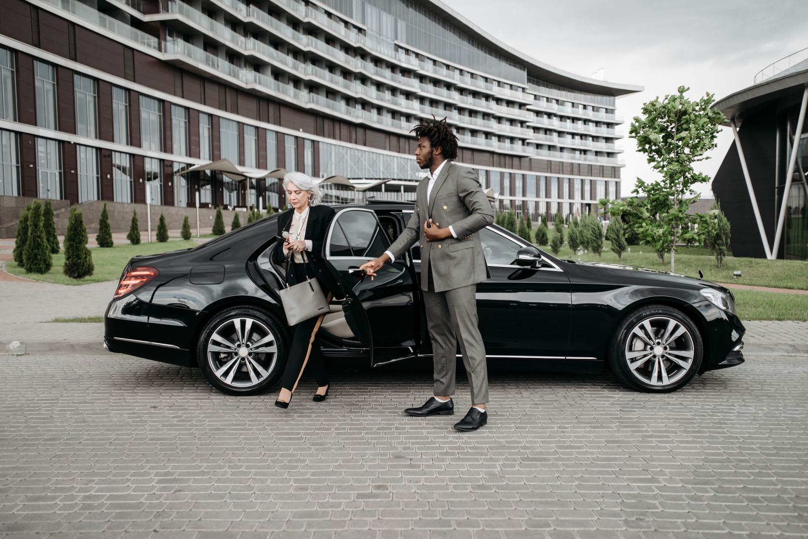 Chauffeur assisting a businesswoman out of a black car outside a hotel