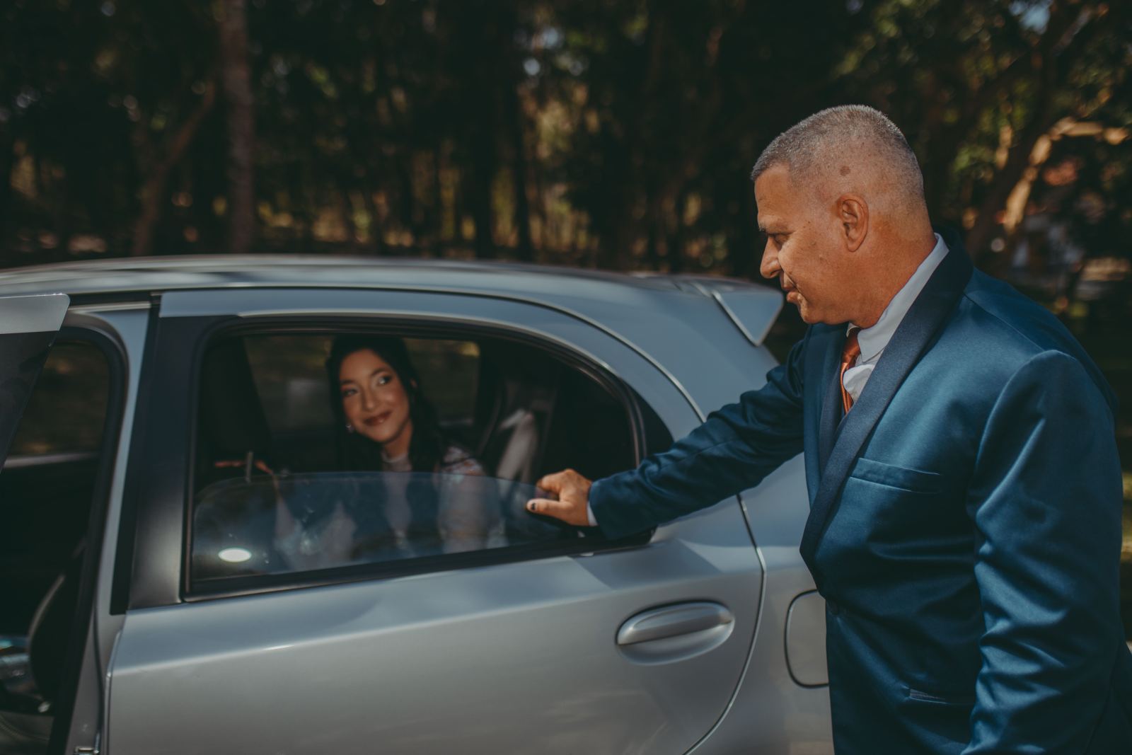 Chauffeur opening the car door for a bride in a forest setting