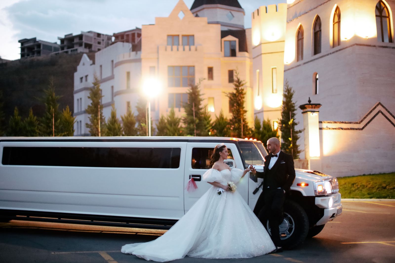 Bride and groom beside a white stretch Hummer limousine at an illuminated venue
