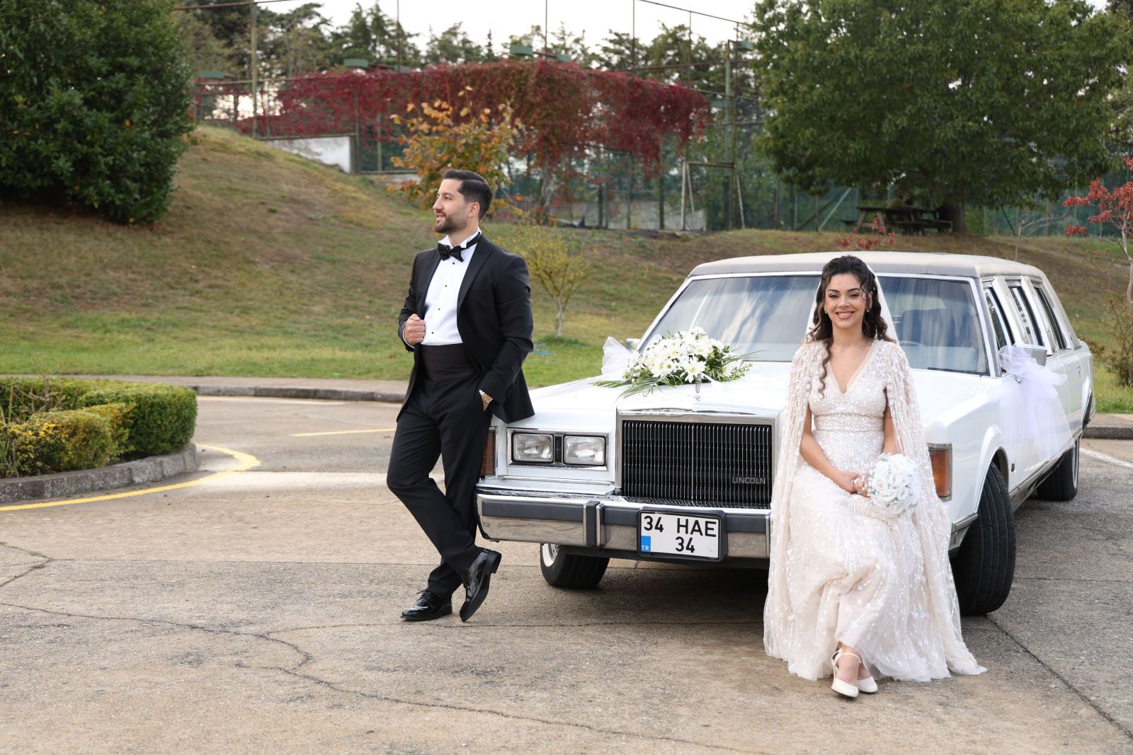 Bride and groom posing beside a white Lincoln stretch limousine in a park