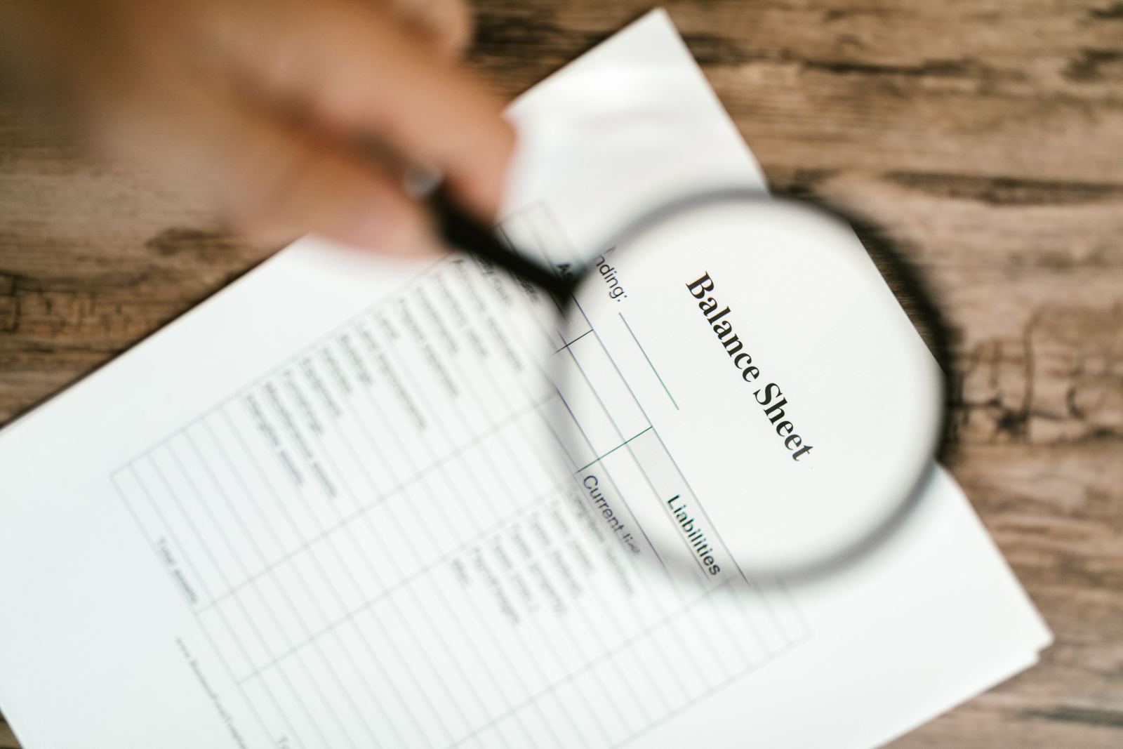 Magnifying glass held over a printed balance sheet document