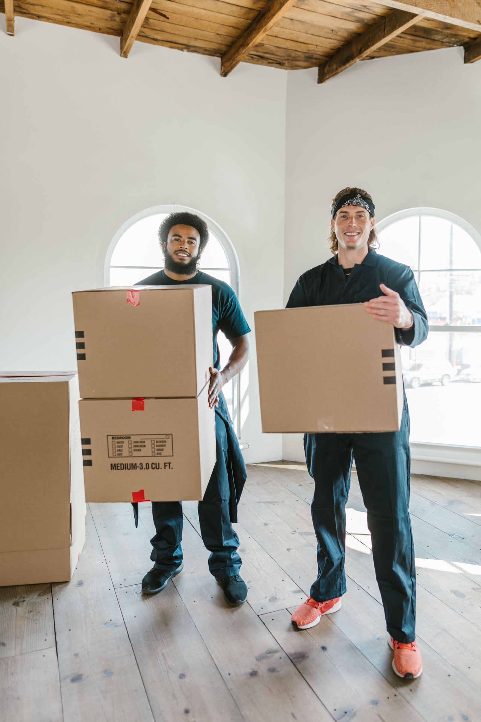 Two smiling movers holding cardboard boxes inside an empty room