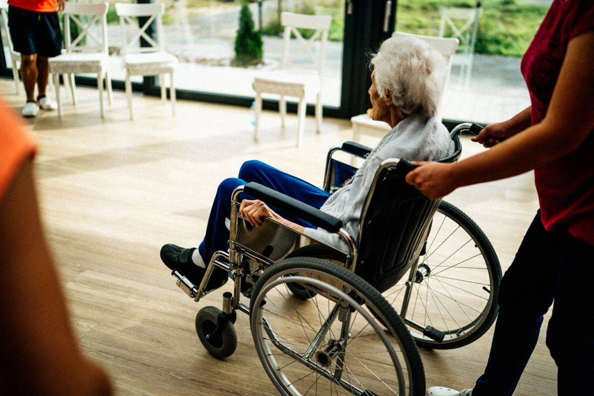 Caregiver pushing a patient in a wheelchair down a care-facility corridor