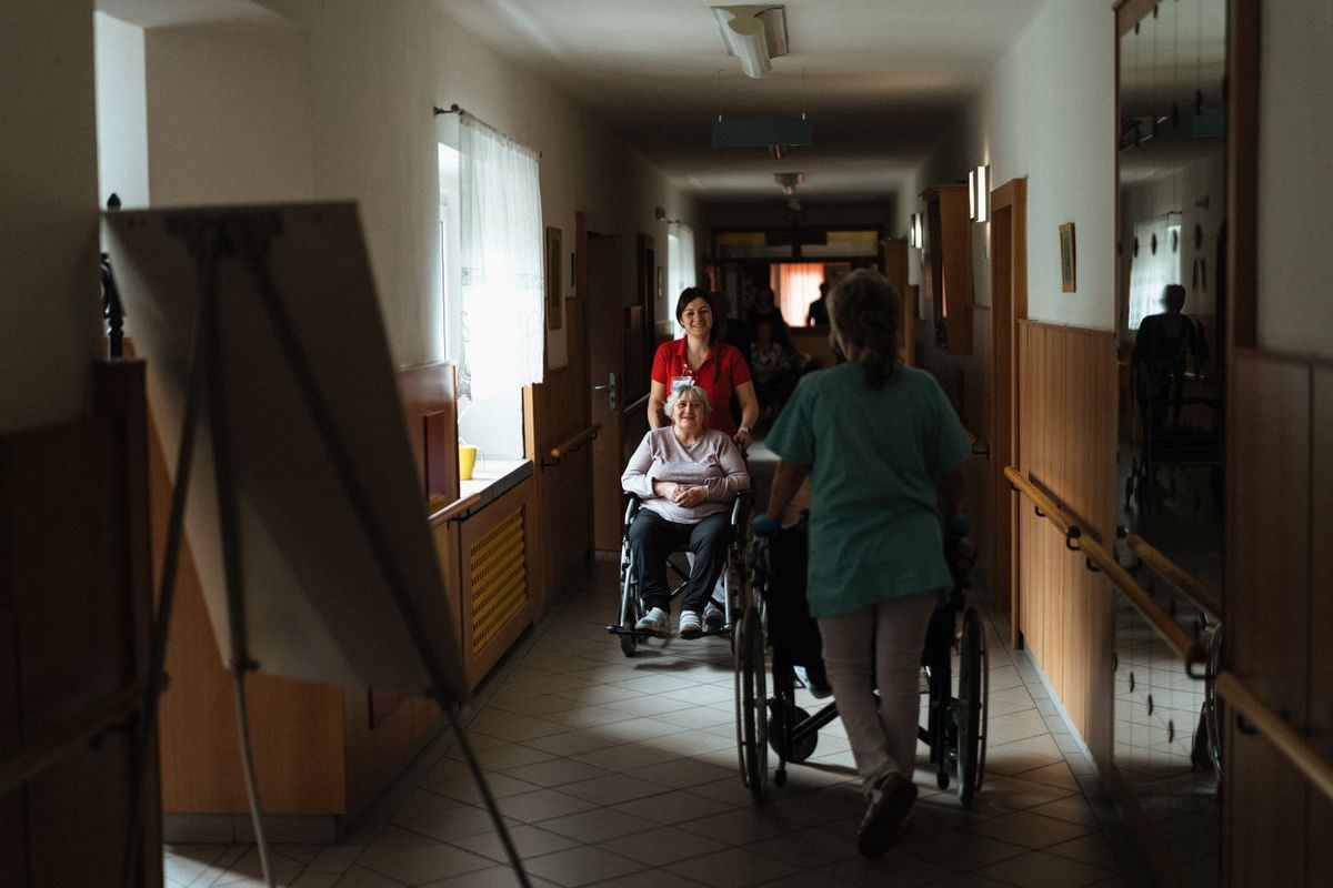 Nurse pushing a senior patient in a wheelchair through a care home hallway