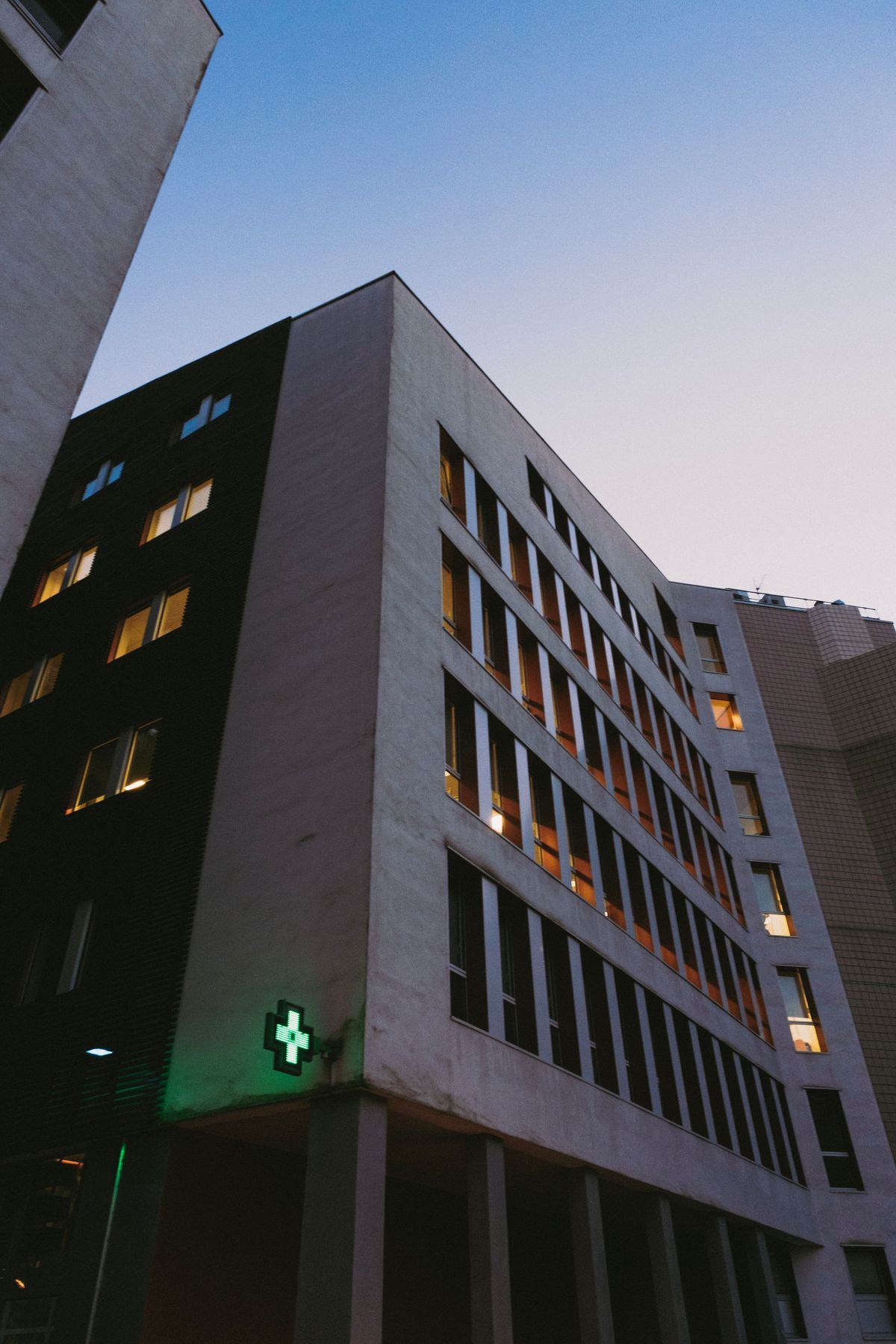 Modern hospital building exterior at dusk with an illuminated medical cross sign