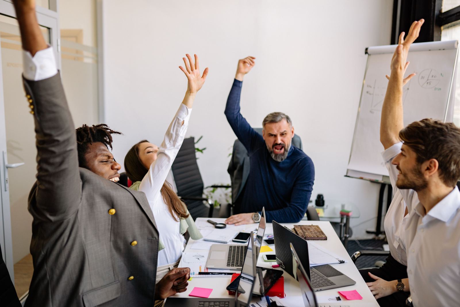 Team of coworkers celebrating with hands raised around a table