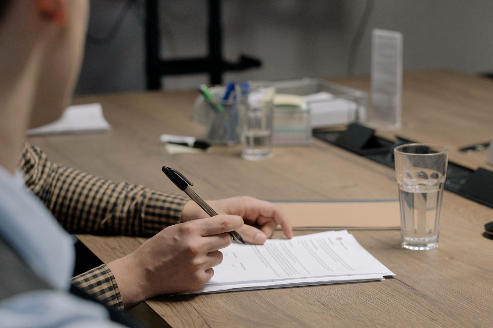 Person signing a printed document at an office desk with a glass of water nearby
