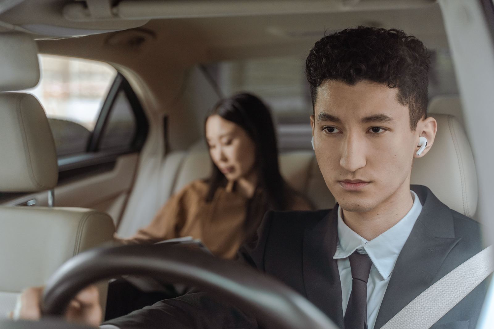 Businessman wearing earbuds driving with a passenger reviewing papers in the back seat