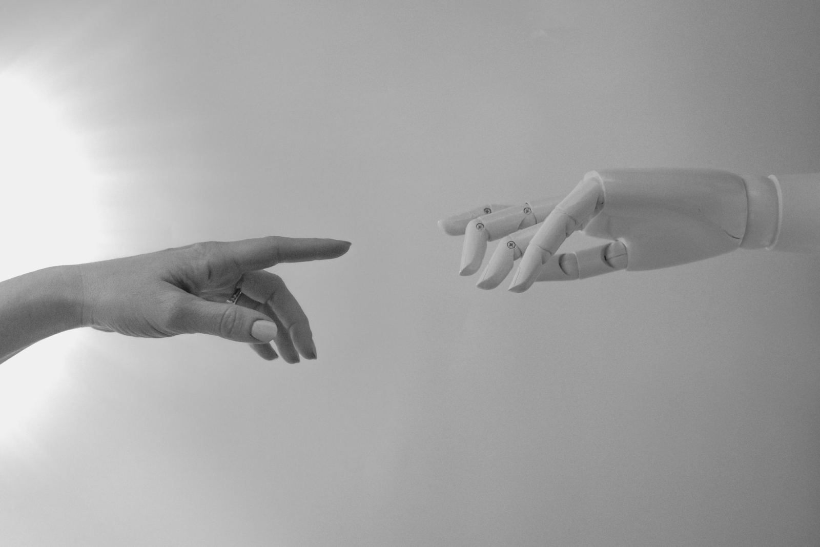 Black-and-white photo of a robotic hand and human hand reaching toward each other