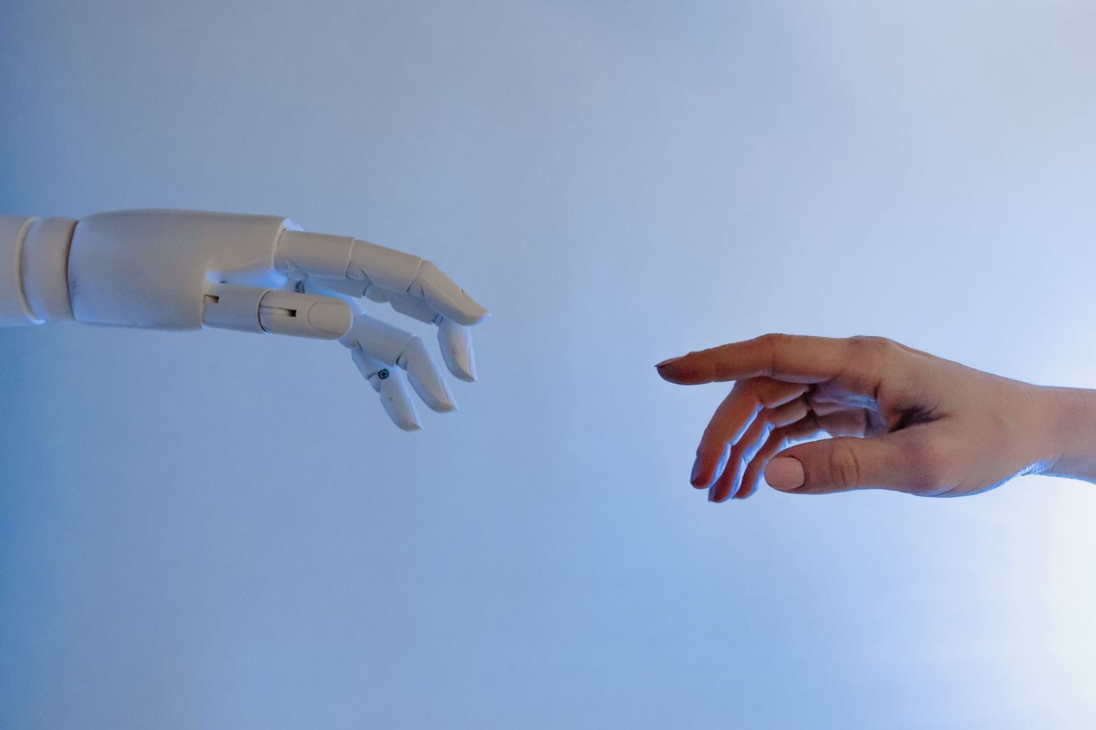 White robotic hand and human hand reaching toward each other against a blue-toned background