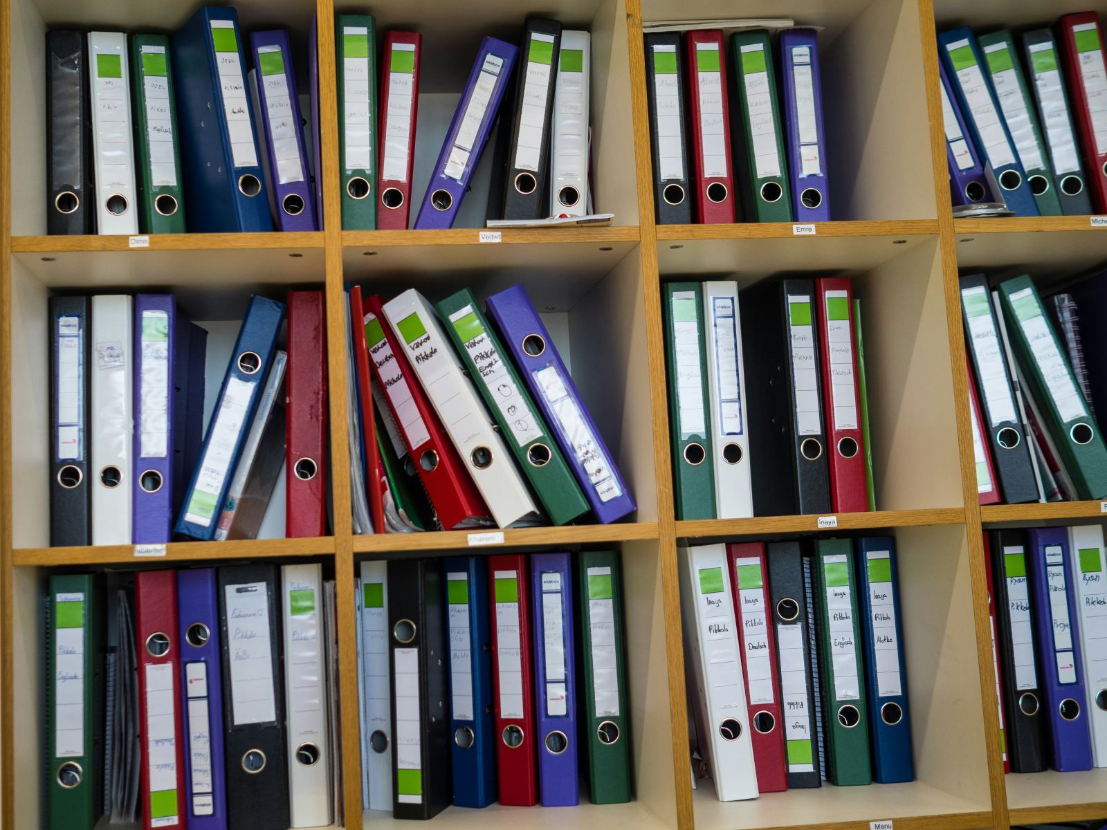 Shelf of colorful ring binders organized and labeled in an office