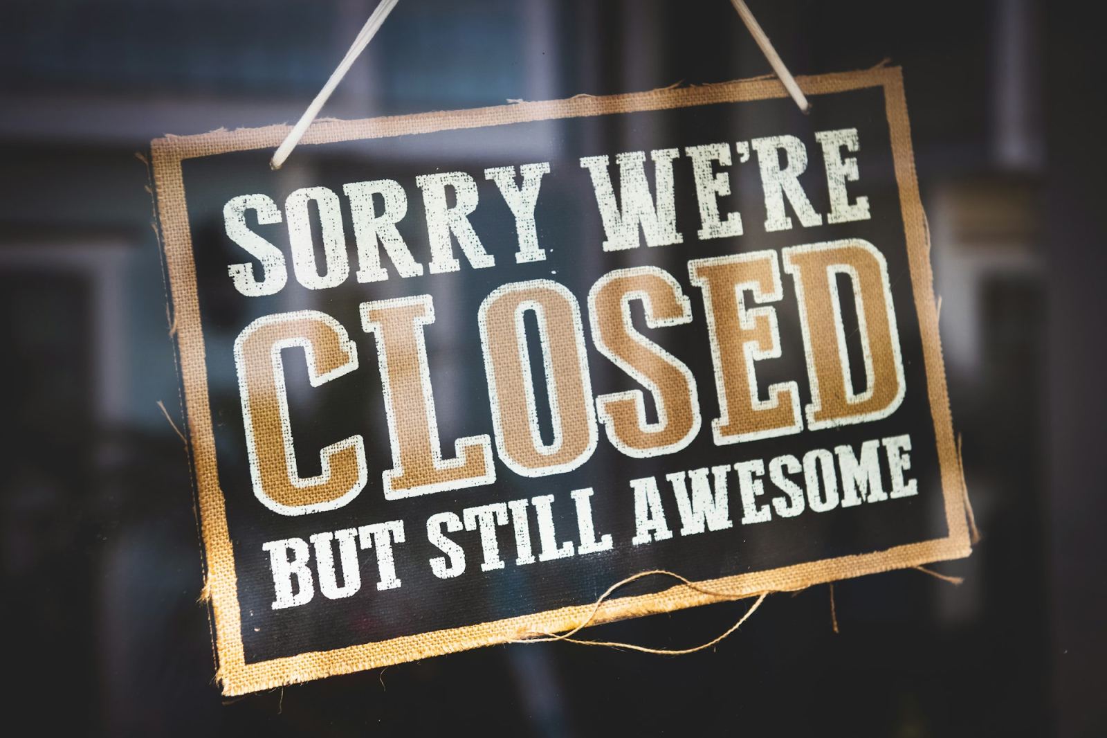 Burlap sign reading Sorry We’re Closed But Still Awesome hanging in a window