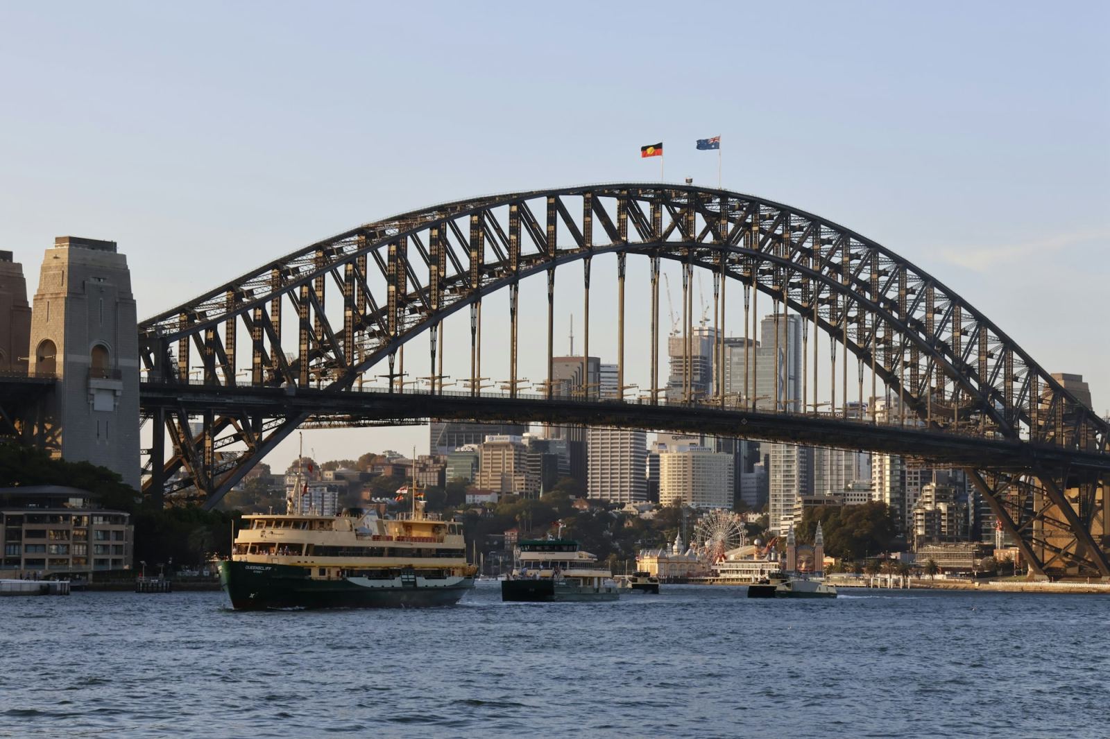 Sydney Harbour Bridge with a ferry passing beneath and flags flying on top