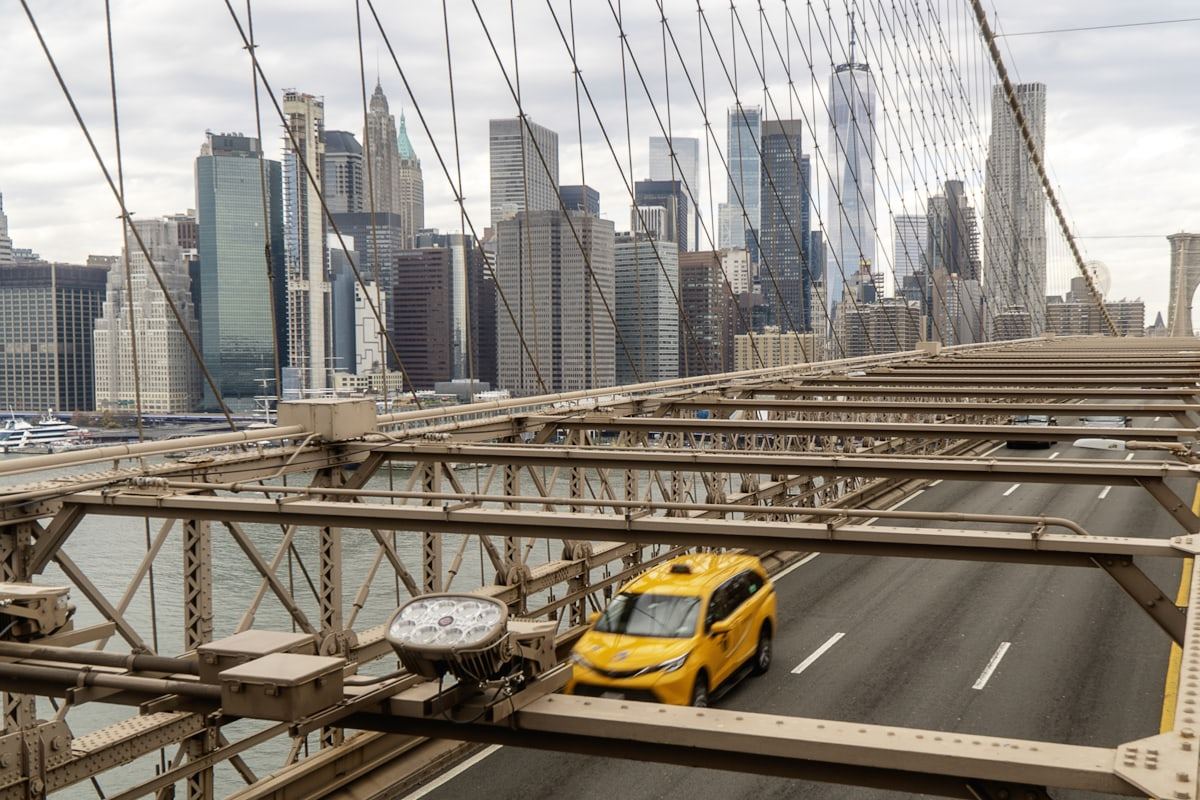 Yellow taxi crossing the Brooklyn Bridge with the Manhattan skyline behind it