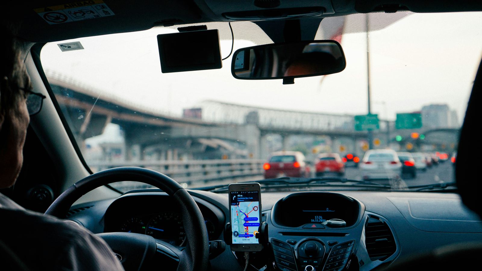 Driver’s view through the windshield with a phone navigation app mounted on the dashboard in traffic