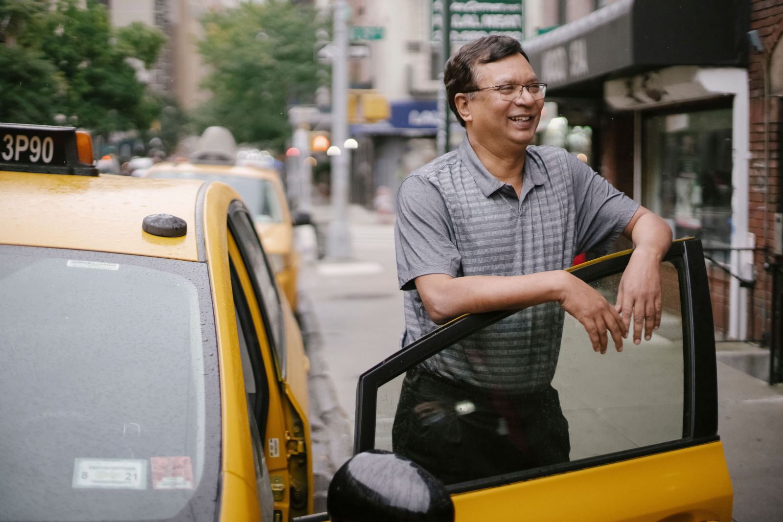 Smiling taxi driver leaning against the open door of his cab