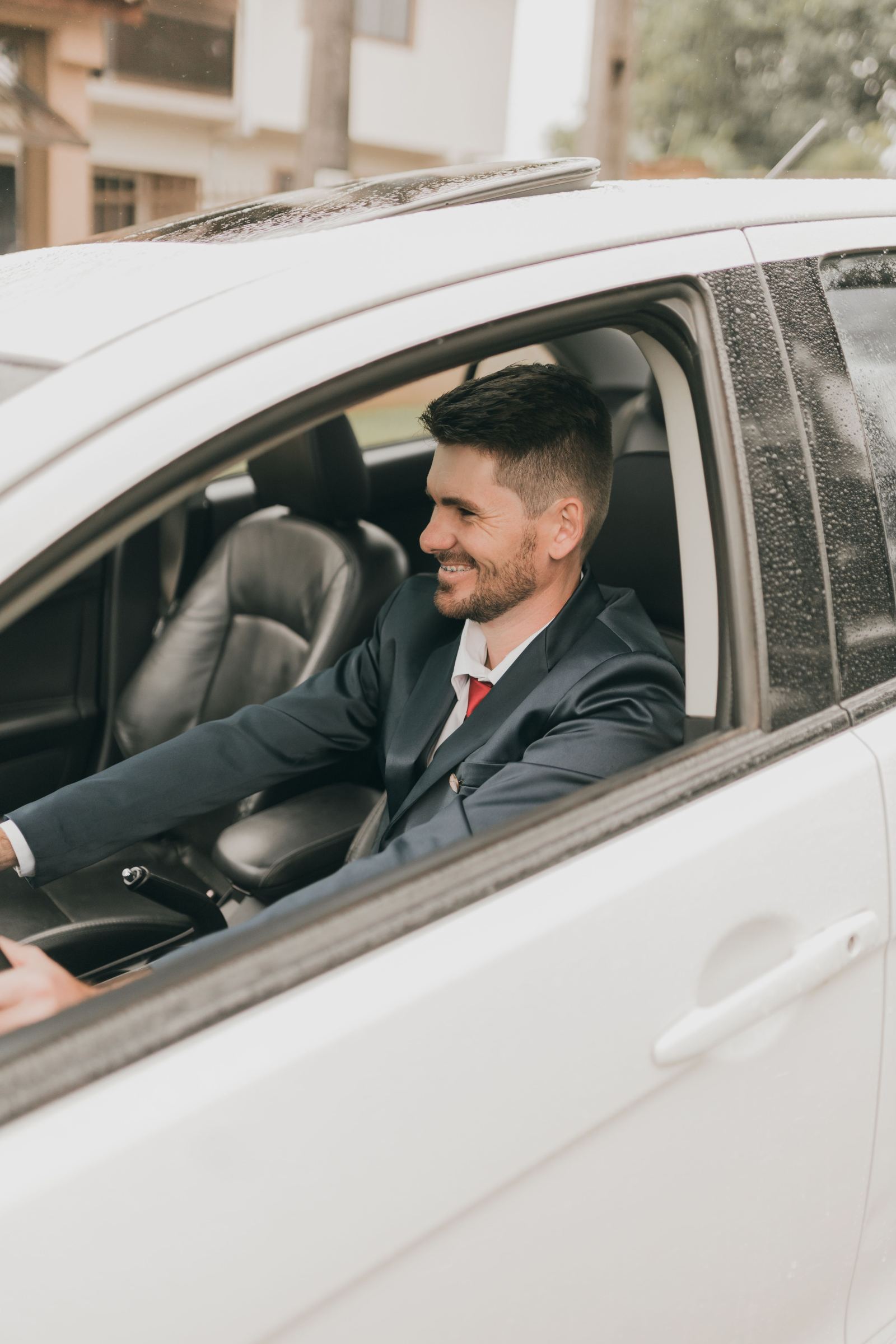 Smiling driver in a suit driving a car in the rain