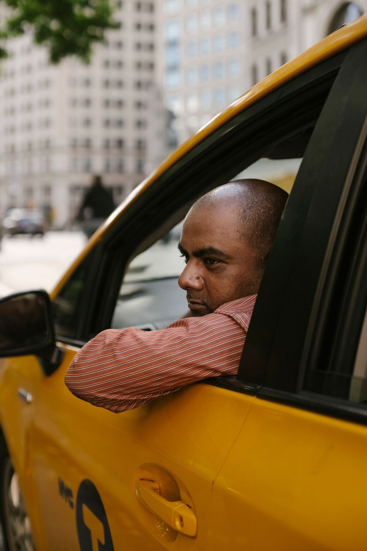 Taxi driver leaning out the window while parked on a city street