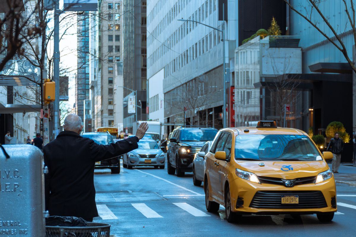 Man hailing a yellow taxi on a busy city street